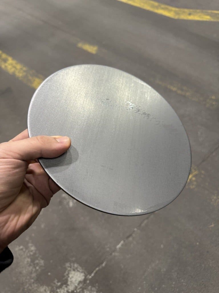 Circular low-carbon steel blank held in hand — starting material for DWI deep drawing process